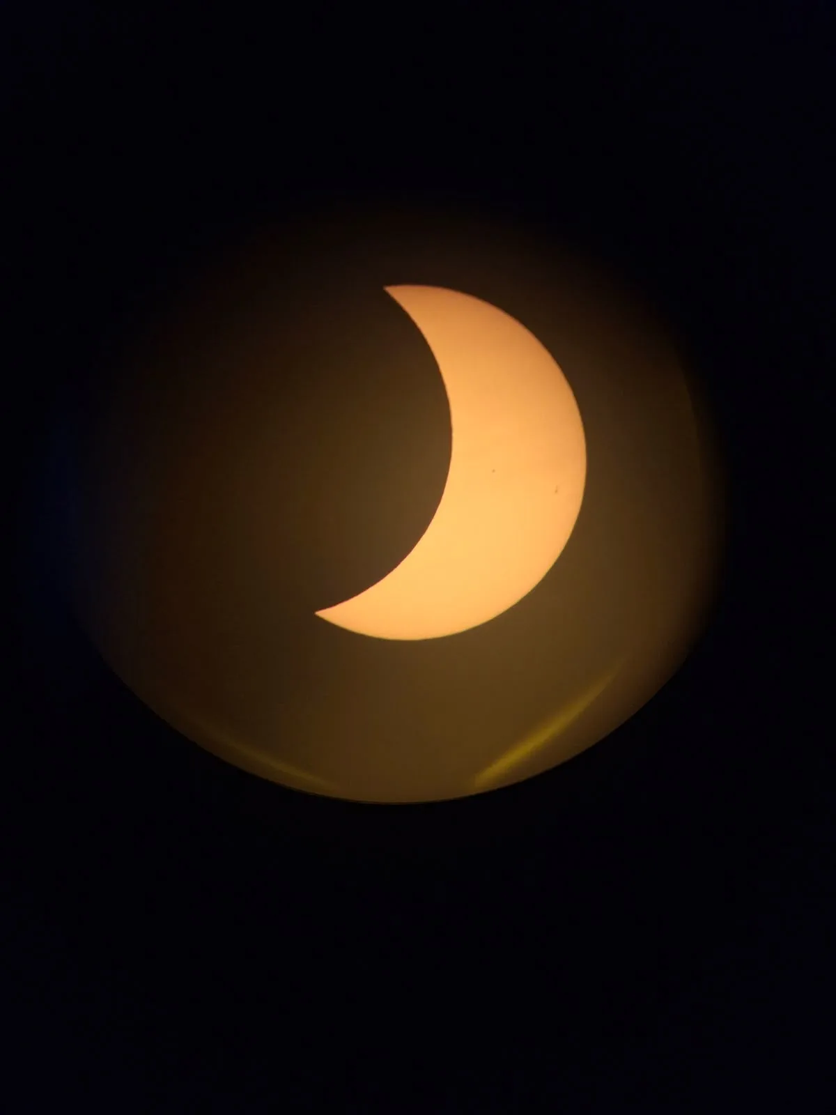 Die verdeckte Sonne als schmale, orange leuchtende Sichel, projiziert auf eine helle Fläche vor dunklem Hintergrund.
